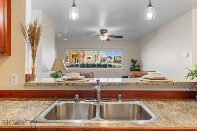 kitchen featuring a sink, hanging light fixtures, ceiling fan, and light stone counters
