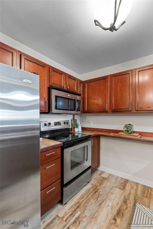 kitchen with brown cabinets, appliances with stainless steel finishes, light wood finished floors, and light countertops