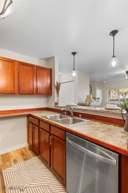 kitchen featuring stainless steel dishwasher, a sink, hanging light fixtures, and light countertops