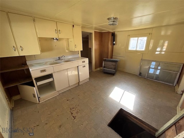 kitchen with brick patterned floor, baseboards, light countertops, white cabinets, and a sink