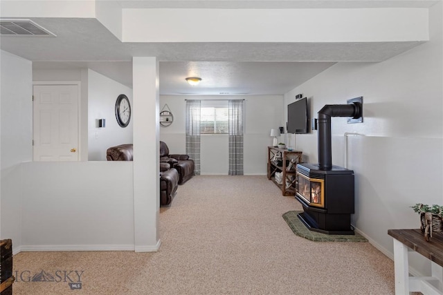 carpeted living area with baseboards, visible vents, and a wood stove