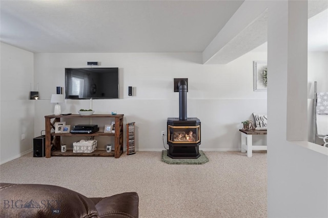 living area featuring baseboards, a wood stove, and carpet flooring
