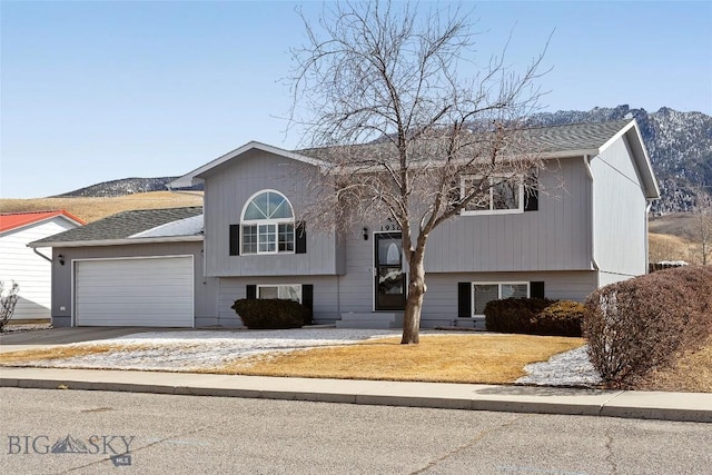 bi-level home featuring an attached garage, driveway, a shingled roof, and a mountain view