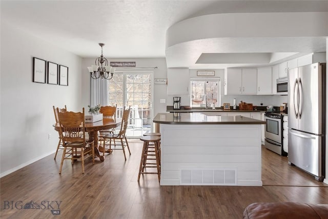 kitchen featuring dark countertops, an inviting chandelier, stainless steel appliances, visible vents, and dark wood-style floors