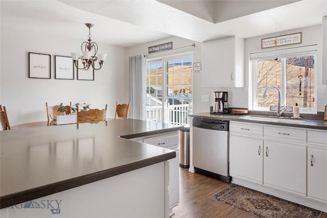 kitchen with dark countertops, stainless steel dishwasher, a sink, an inviting chandelier, and white cabinetry