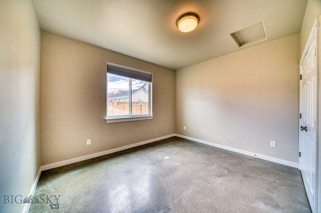 unfurnished room with baseboards, attic access, and concrete floors