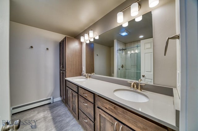 bathroom with a sink, baseboard heating, a tile shower, and double vanity