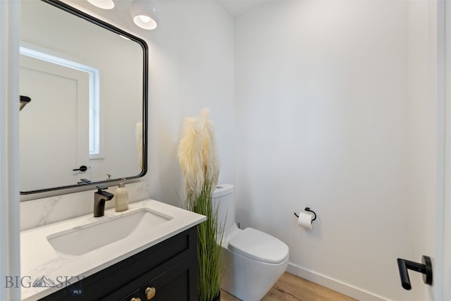 half bath with vanity, baseboards, toilet, and wood finished floors
