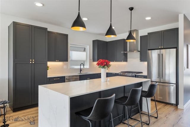 kitchen featuring a kitchen bar, a sink, stainless steel appliances, light wood-type flooring, and decorative light fixtures