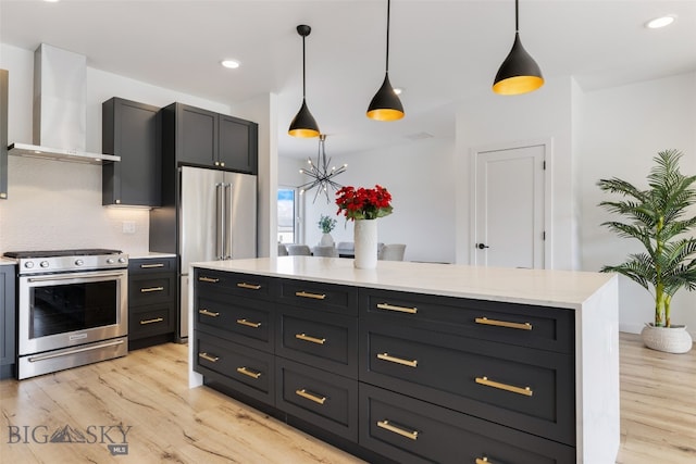 kitchen with wall chimney range hood, light wood finished floors, appliances with stainless steel finishes, and decorative light fixtures