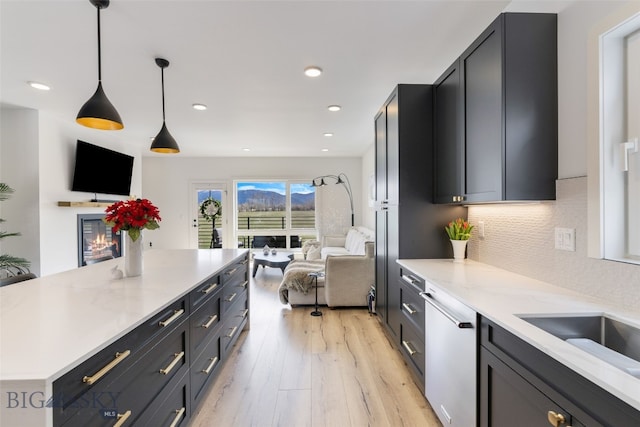 kitchen featuring light stone countertops, stainless steel dishwasher, open floor plan, backsplash, and light wood-type flooring