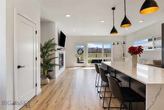 kitchen with pendant lighting, light wood-style flooring, open floor plan, a lit fireplace, and baseboards