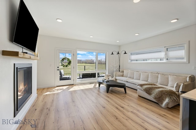 living room featuring recessed lighting, light wood-style floors, baseboards, and a glass covered fireplace