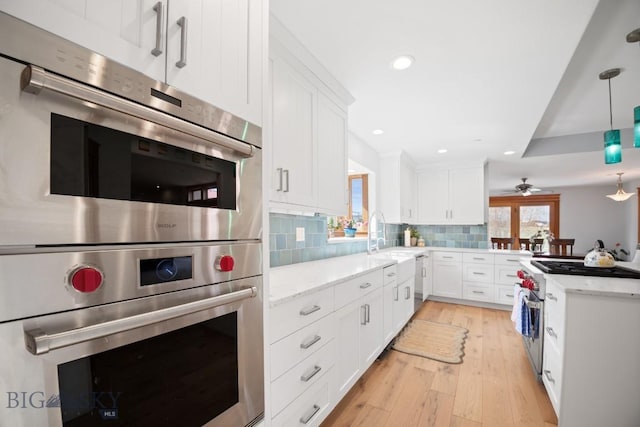 kitchen featuring white cabinets, light stone counters, double oven, light wood-type flooring, and backsplash