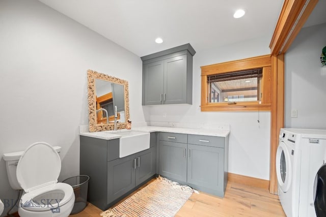 clothes washing area featuring cabinet space, a sink, light wood-style floors, baseboards, and washer / dryer