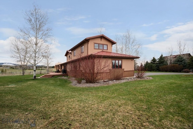 back of property with a lawn, stucco siding, and metal roof