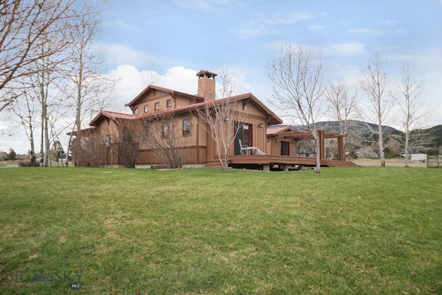 rear view of property featuring a lawn, a wooden deck, and a chimney
