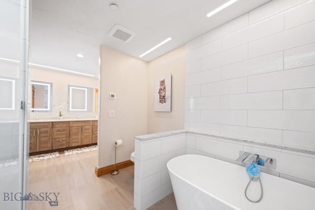 bathroom with double vanity, tile walls, baseboards, toilet, and a soaking tub