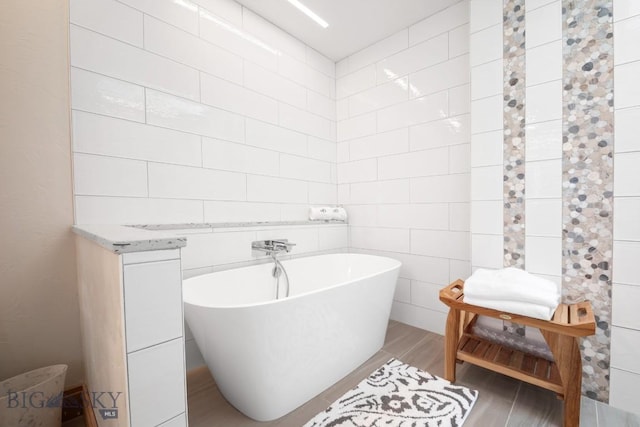 full bathroom with a freestanding tub, tile walls, and wood finished floors