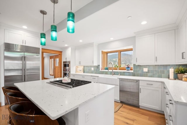 kitchen with a breakfast bar area, a center island, a sink, stainless steel appliances, and white cabinetry