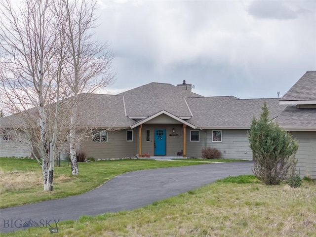 ranch-style home with roof with shingles, a chimney, and a front lawn