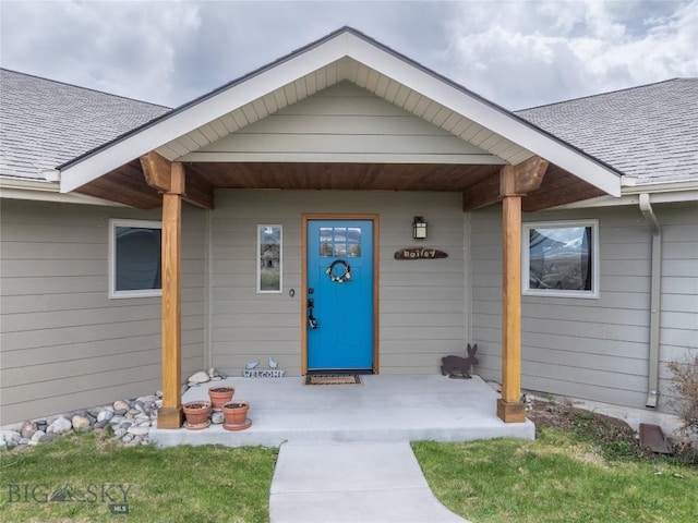 entrance to property with covered porch and a shingled roof