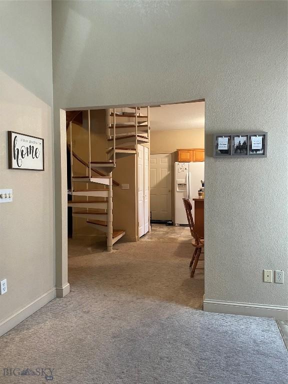 93 8th St Unit B, Belgrade, MT 59714 - below grade area with a textured wall, white refrigerator with ice dispenser, stairs, and light colored carpet