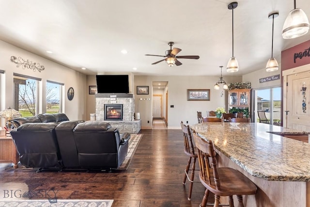 living area featuring a ceiling fan, a fireplace, baseboards, recessed lighting, and dark wood-type flooring