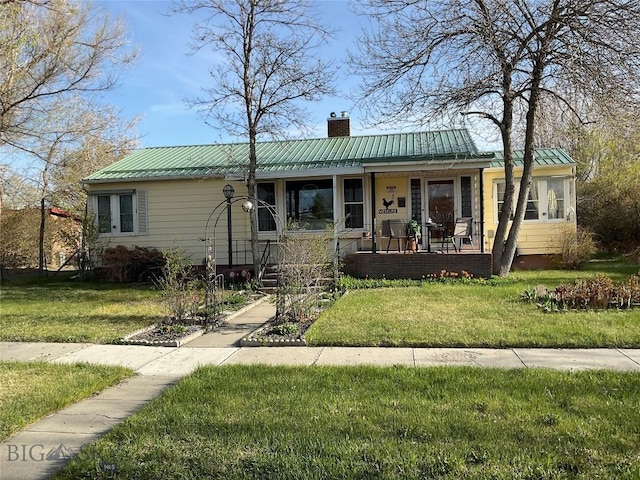 ranch-style house featuring a front yard, covered porch, a chimney, and metal roof