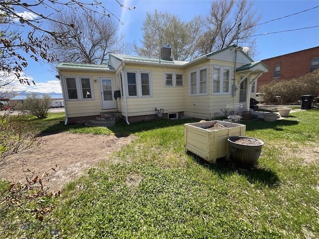 back of property with a yard, a chimney, metal roof, and entry steps