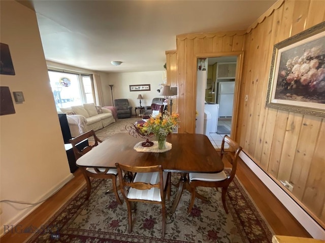 dining space featuring a baseboard heating unit, wood finished floors, and wooden walls