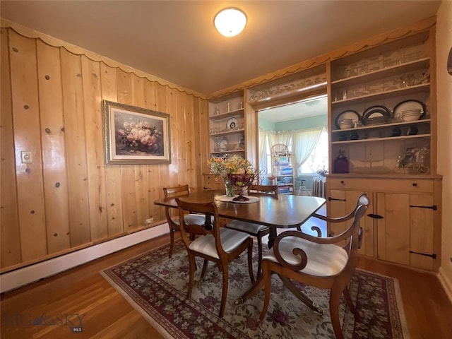 dining space with wood walls, dark wood finished floors, and a baseboard heating unit
