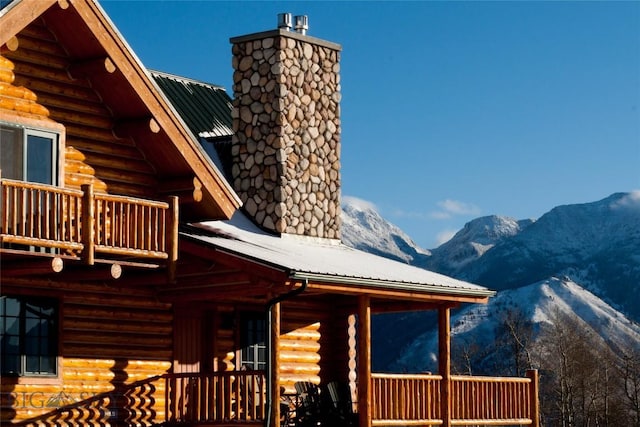 view of property exterior featuring log exterior, a mountain view, a balcony, and a chimney