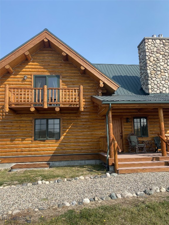 rear view of house with log exterior, a balcony, and a chimney