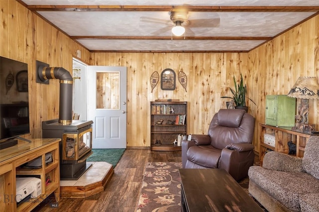 living room with wooden walls, beamed ceiling, a wood stove, and wood finished floors