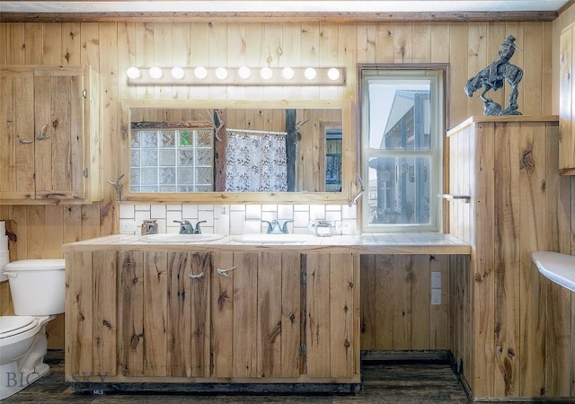 bathroom with wooden walls, double vanity, toilet, and a sink