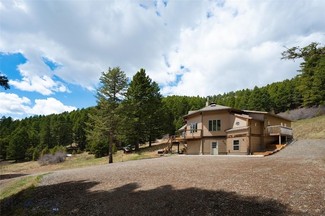 189 Quinn Creek Rd, Bozeman, MT 59715 - back of house with a chimney, a deck, a view of trees, driveway, and stairs