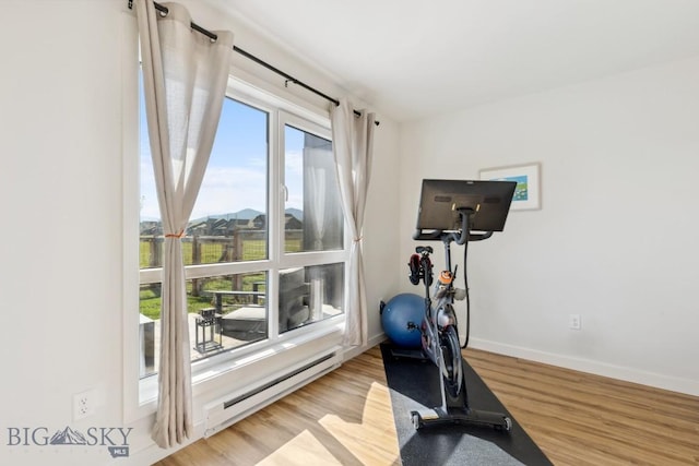 workout room with wood finished floors, baseboards, and a baseboard heating unit