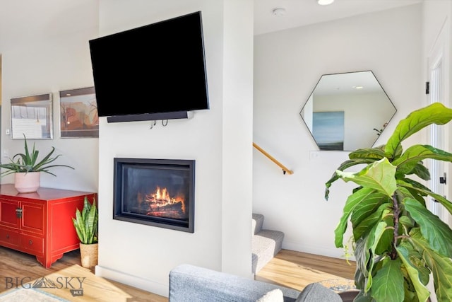 living area featuring stairs, baseboards, a glass covered fireplace, and wood finished floors