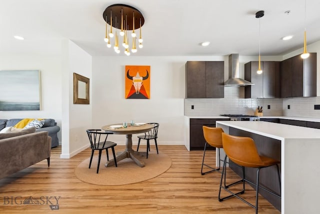 kitchen with light countertops, wall chimney exhaust hood, dark brown cabinetry, and a kitchen bar