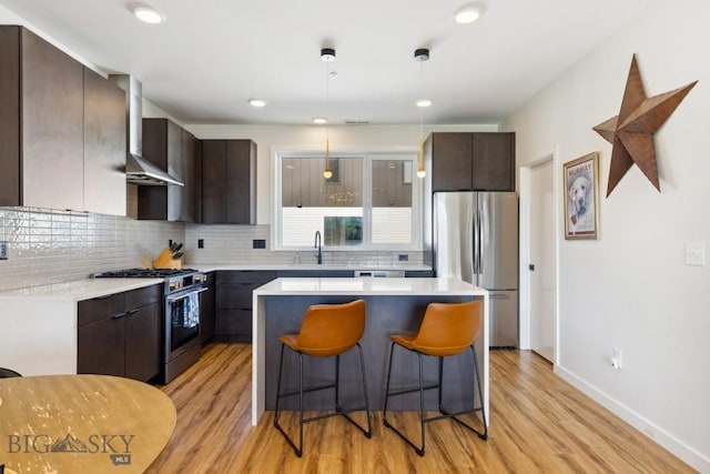 kitchen featuring light wood-type flooring, wall chimney range hood, appliances with stainless steel finishes, and dark brown cabinetry