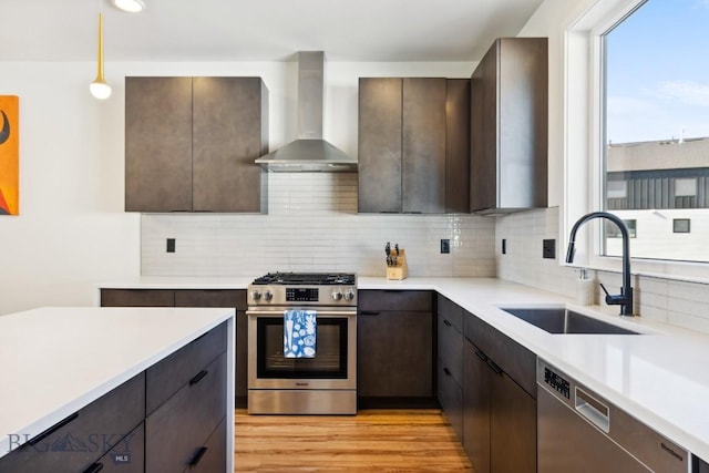 kitchen featuring wall chimney range hood, stainless steel appliances, a sink, and dark brown cabinetry