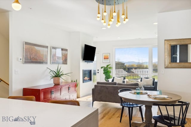 dining area with light wood finished floors, recessed lighting, a chandelier, and a glass covered fireplace