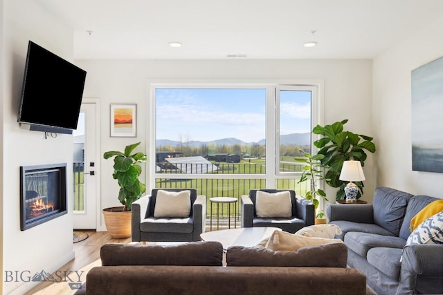 living room featuring recessed lighting, a mountain view, a glass covered fireplace, and wood finished floors