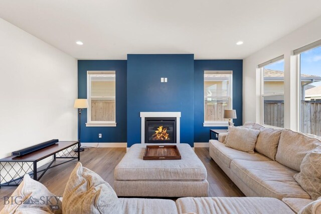 living area featuring recessed lighting, baseboards, a glass covered fireplace, and wood finished floors