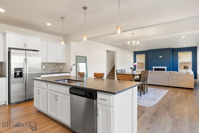 kitchen with a sink, tasteful backsplash, an island with sink, dark countertops, and appliances with stainless steel finishes
