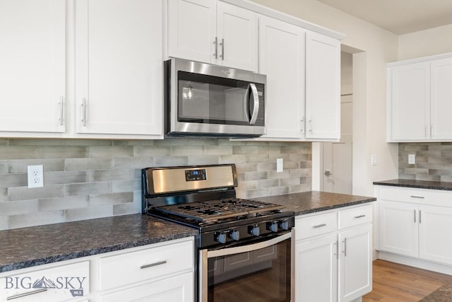 kitchen with light wood finished floors, dark stone counters, stainless steel appliances, white cabinets, and backsplash
