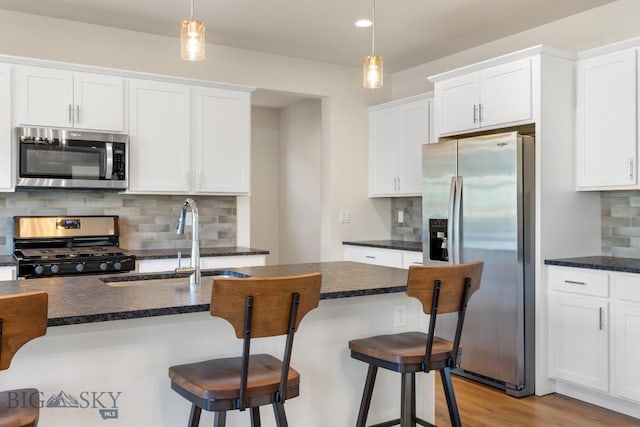 kitchen with a sink, a kitchen bar, decorative backsplash, white cabinets, and appliances with stainless steel finishes
