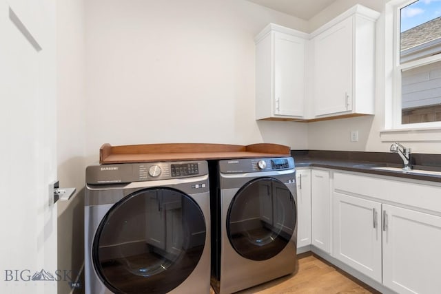 clothes washing area featuring a sink, separate washer and dryer, light wood-type flooring, and cabinet space