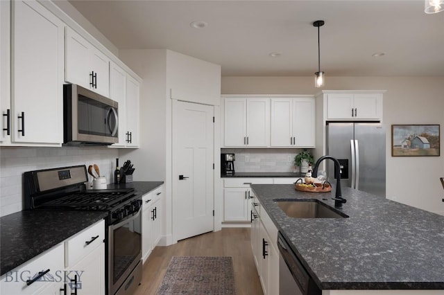 kitchen with appliances with stainless steel finishes, a sink, wood finished floors, tasteful backsplash, and an island with sink
